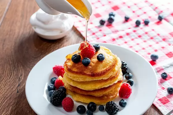 Pouring honey onto tasty pancakes with berries on table, closeup (Flip 2019)
