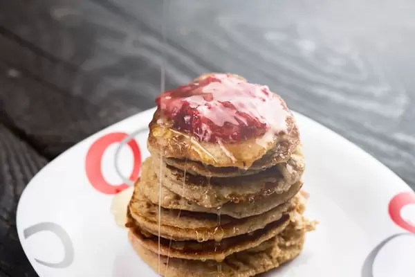Pouring organic honey to freshly baked pancakes with fruit jam. Healthy gluten-free snack