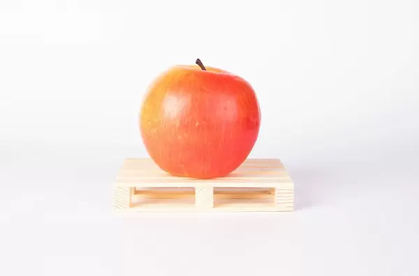 Praller roter Apfel auf kleiner Holzpalette als Symbol für Transport von Früchten und Gemüse