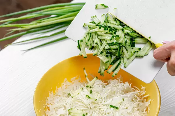 Preparation of cabbage salad. Female hand pour sliced cucumbers into a bowl (Flip 2019)