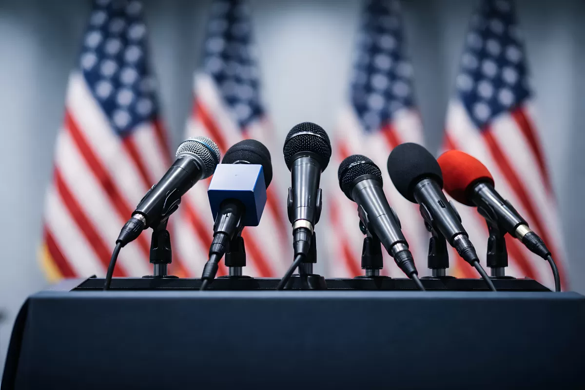 Pressekonferenz mit Mikrofonen und US-Flaggen