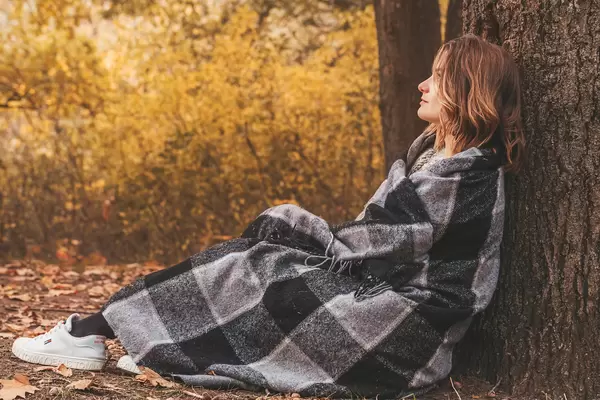 Pretty woman wrapped herself in a blanket and sits under a tree