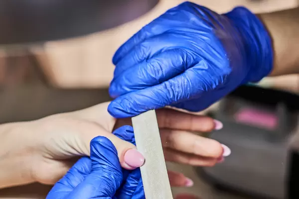 Professional manicure master in blue gloves shortening nails