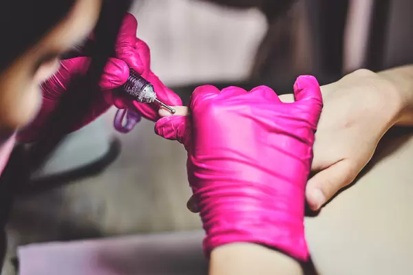 Professional manicure master using an electric nail file to remove cuticles in the beauty salon