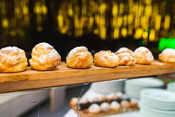 Profiteroles Windbeutel mit Sahne gefüllt auf einer Ablage mit Goldenen Lichtern im Hintergrund