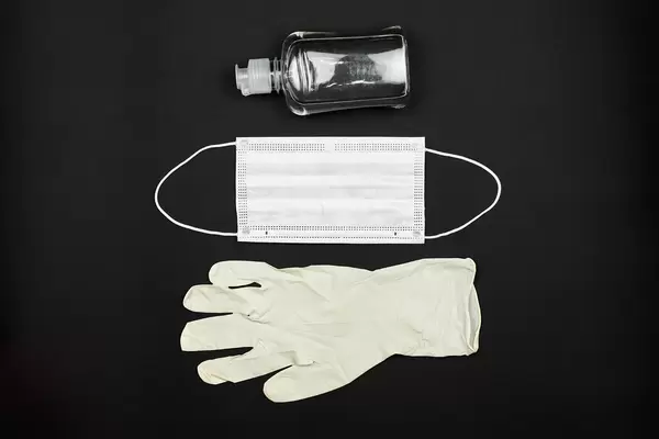Protective medical gloves, face mask and antiseptic gel on dark background
