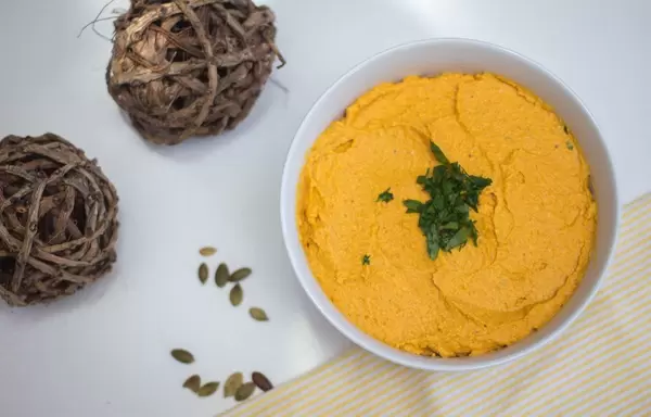Pumpkin hummus in a bowl with parsley and punpkin seeds aside - top view
