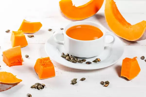Pumpkin orange soup with slices of fresh pumpkin and seeds on white wooden background