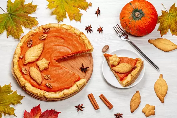 Pumpkin pie with autumn decorations on white wooden table. Top view