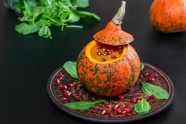 Pumpkin puree and pomegranate in fresh pumpkin with spinach leaves on black background