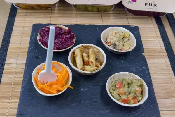 PUR - veganer Bio Nudelsalat, Quinoasalat und Rote Betesalat als Proben in Schälchen auf einer Messer