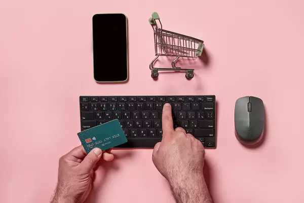 Purchasing products in online store - a man holding credit card and typing numbers on the keyboard