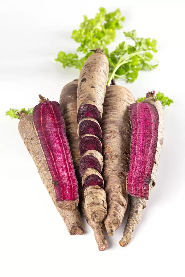 Purple carrots, whole and sliced on white plate with green leaves