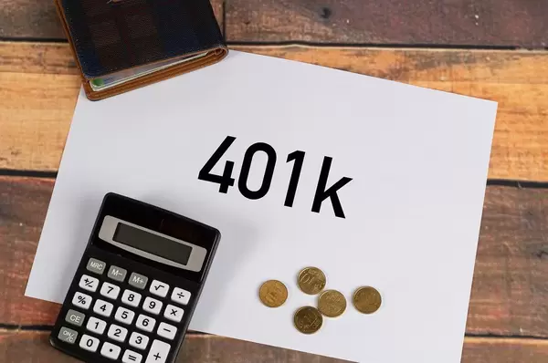 "401 k"  auf weißem Papier geschrieben, neben einem Taschenrechner, Kleingeld aus Eurocent-Münzen und einer Geldbörse