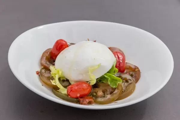 "Burrata" Mozarella-Salat mit Tomatenkompott un Gurken auf einem weißen Teller im Hotel 1898 auf den La Ramblas in Barcelona, Spanien