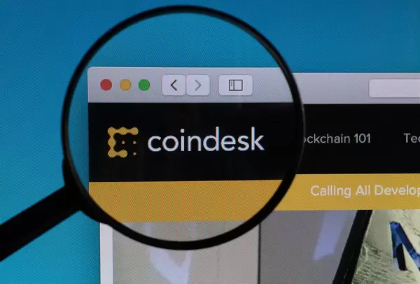 "Coindesk" Schriftzug und Logo, vergrößert durch ein Lupenglas dargestellt