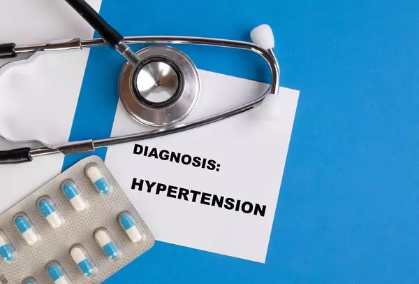 "Diagnose: Bluthochdruck", geschrieben auf blauem Ärzteordner, neben Medikamenten und Stethoskop