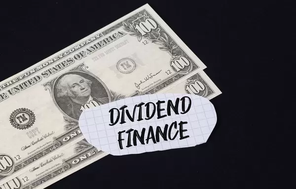 "Dividend finance" Text auf kariertem Zettel mit zwei 100-Dollar-Scheinen vor schwarzem Hintergrund
