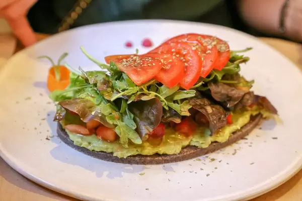 "Petit Pa with tomatoes" is a raw bread made wit sunflower and flax seeds, green leaves topping and avocado at Petit Brot in Barcelona, Spain
