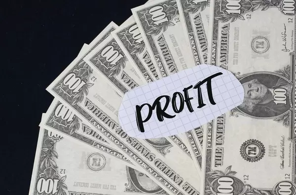 "Profit" Text auf kariertem Zettel mit 100-Dollar-Scheinen