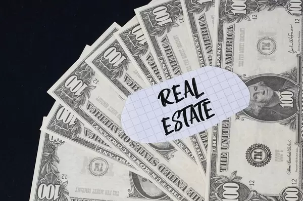 "Real estate" Text auf kariertem Zettel mit 100-Dollar-Scheinen