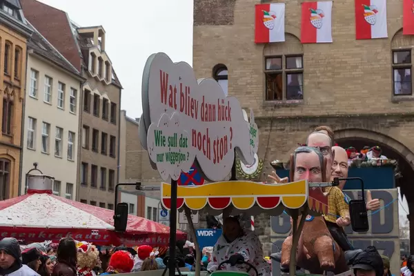 "Wie soll dat nur wiggerjon? Wat bliev dann hück noch ston? Die Hüsjer un Jasse,": einige Zeilen vom Lied "En unserem Veedel" von Bläck Fööss vor dem Persiflagewagen beim Rosenmontagsumzug in Köln