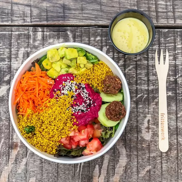 Rainbow Bowl: bunter Spinat-Mix, Avocadowürfel, Pink Hummus, Falafelbällchen, Gurkenscheiben, Quinoa, Karottenstreifen, Tomatenwürfel, Sauce