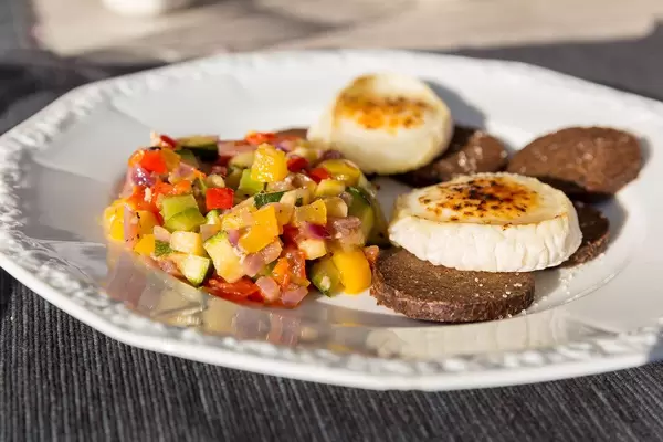 Ratatouille, Pumpernickel und flambierter Käse auf einem weißen Teller