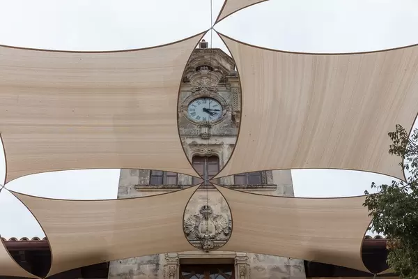 Rathaus von Alcudía: die Uhr und das Wappen an der Fassade von großen Schattensegeln eingerahmt