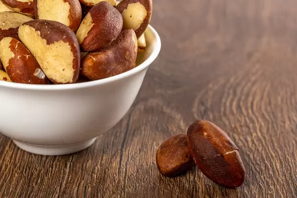 Raw brazil nuts in white bowl on wooden background