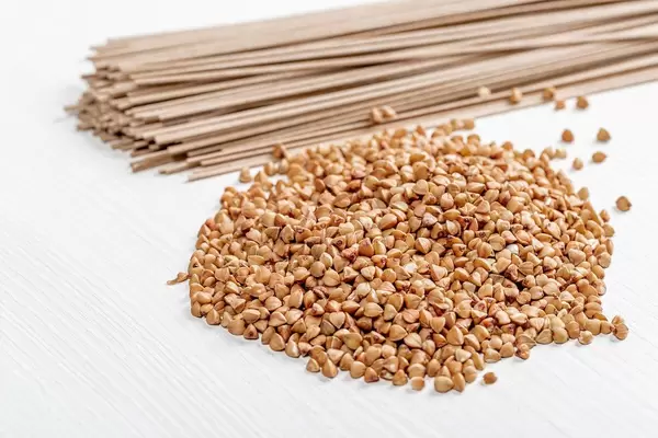 Raw buckwheat and buckwheat soba noodles on white wooden background