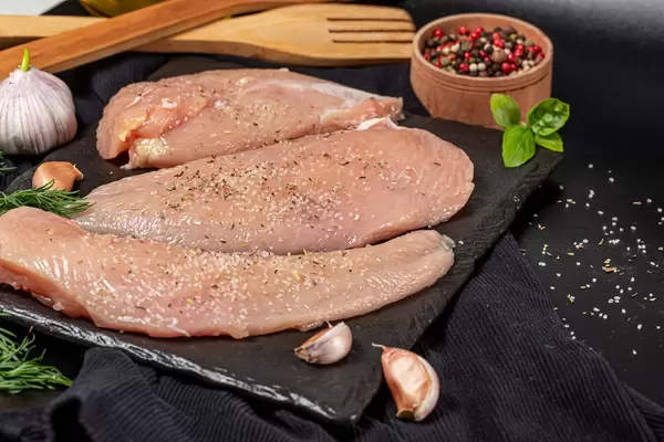 Raw chicken fillet with spices on dark background