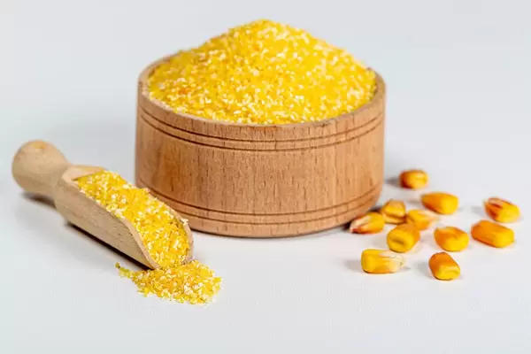 Raw corn grits in a wooden bowl and scoop on a white background