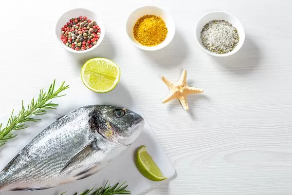 Raw fresh Dorada on a white wooden table with spices, rosemary, lime slices and starfish