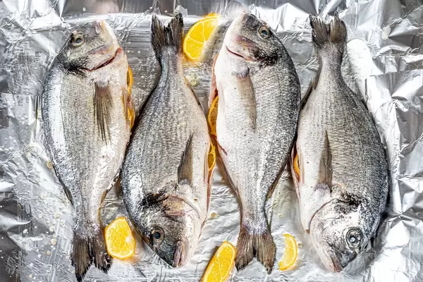 Raw fresh Dorado with spices and lemon slices on foil. Top view (Flip 2020)