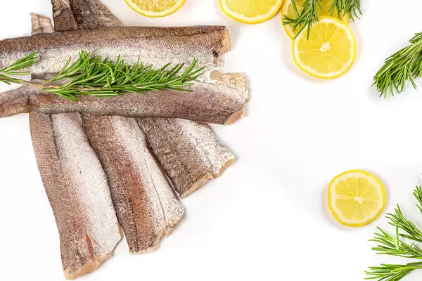 Raw hake fish fillet on white background with lemon and rosemary