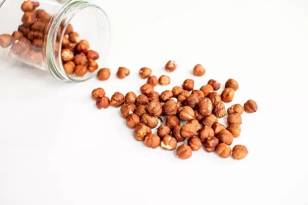 Raw hazelnuts in glass jar on white background
