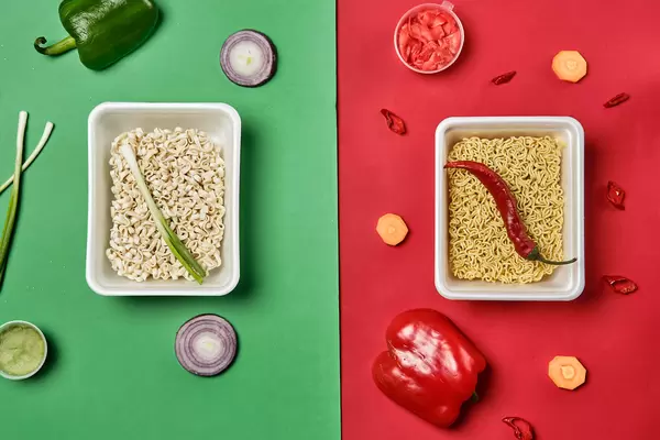 Raw instant food noodles in containers with various ingredients on colored background