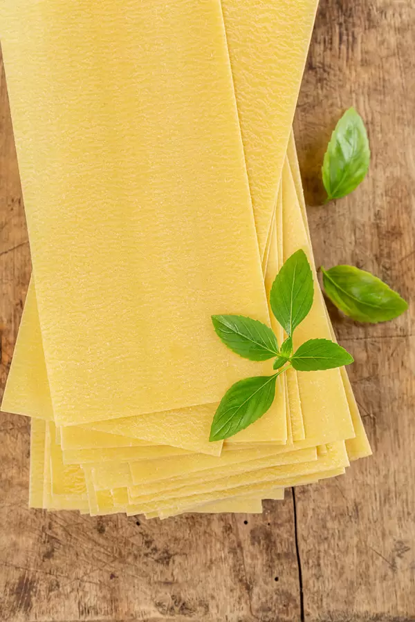 Raw lasagna sheets with basil leaves on wooden background, top view
