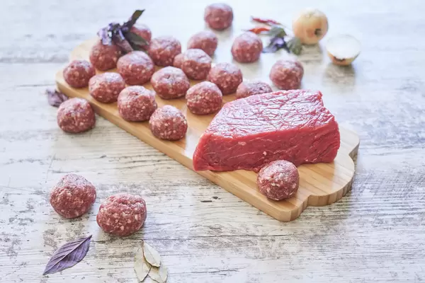 Raw meatballs and a slice of beef fillet on a wooden plate
