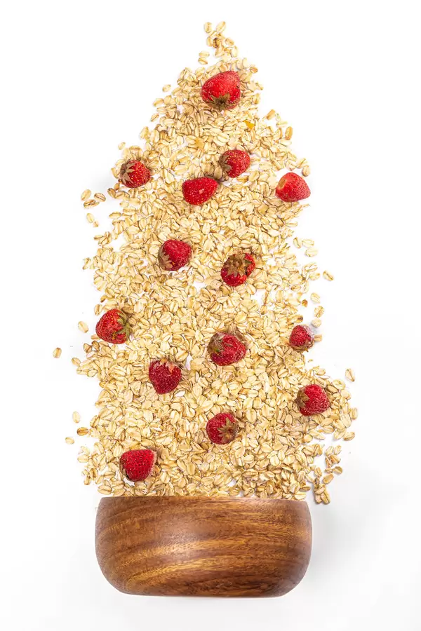 Raw oatmeal with fresh strawberries scattering on white from a wooden bowl