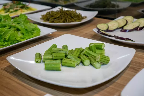 Raw Okra, Zucchini, Lettuce and Pickled Water Spinach on White Plates at a Buffet in a Restaurant