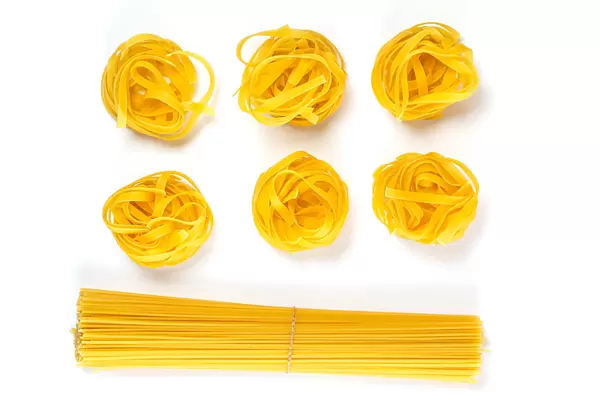 Raw pasta nest and spaghetti on a white background, top view