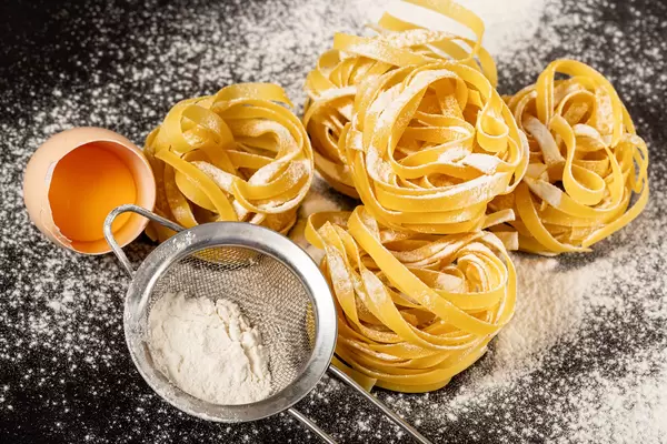 Raw pasta with flour and broken egg on black background
