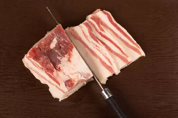 Raw pork belly pieces on a brown cutting board
