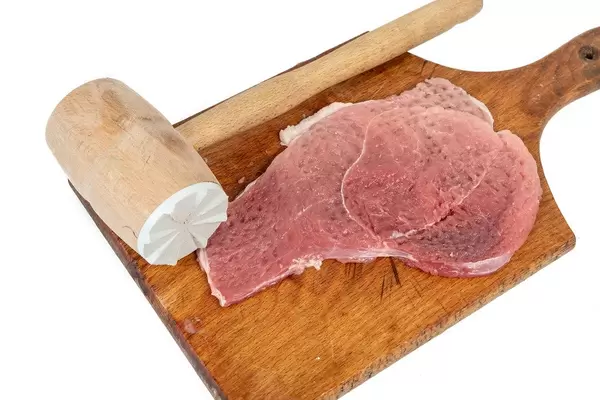 Raw Pork Chops on the board with wooden hammer