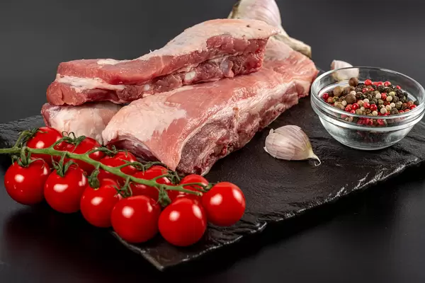Raw ribs on black background with tomato, garlic and pepper
