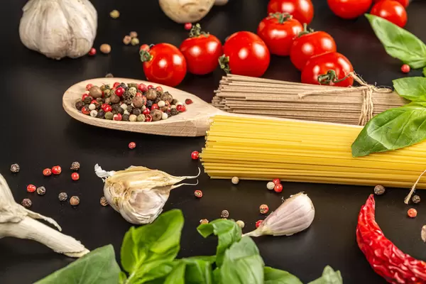 Raw spaghetti and buckwheat noodles on black background with ingredients
