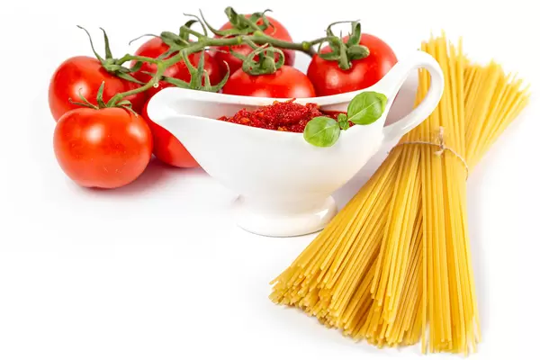 Raw spaghetti with tomatoes and sauce on a white background