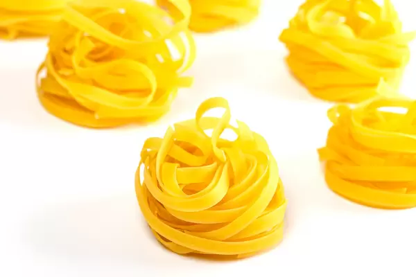 Raw tagliatelle pasta on white background